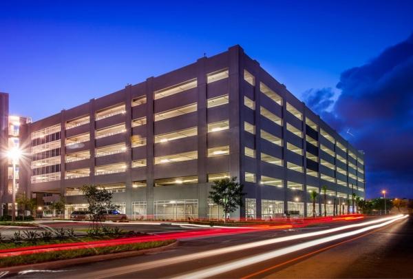 Exterior photo of the 迈阿密 Dade College Hialeah Campus parking garage. Evening photo with bright blue skies. 车库灯亮着. Vehicle lights create streaks on the adjacent street.