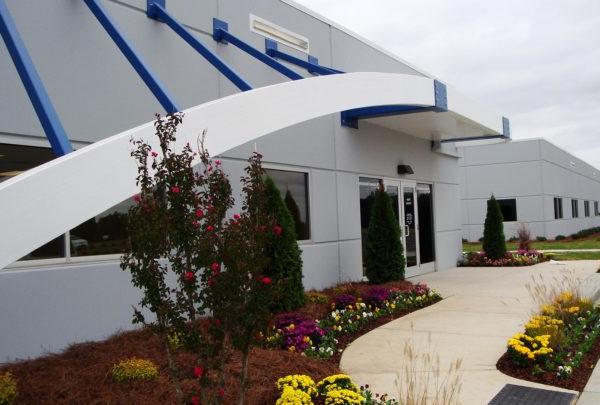 Front entrance of Turbomeca TMM 澳门足彩app Facility. Awning supported by blue structures. Floral landscaping.